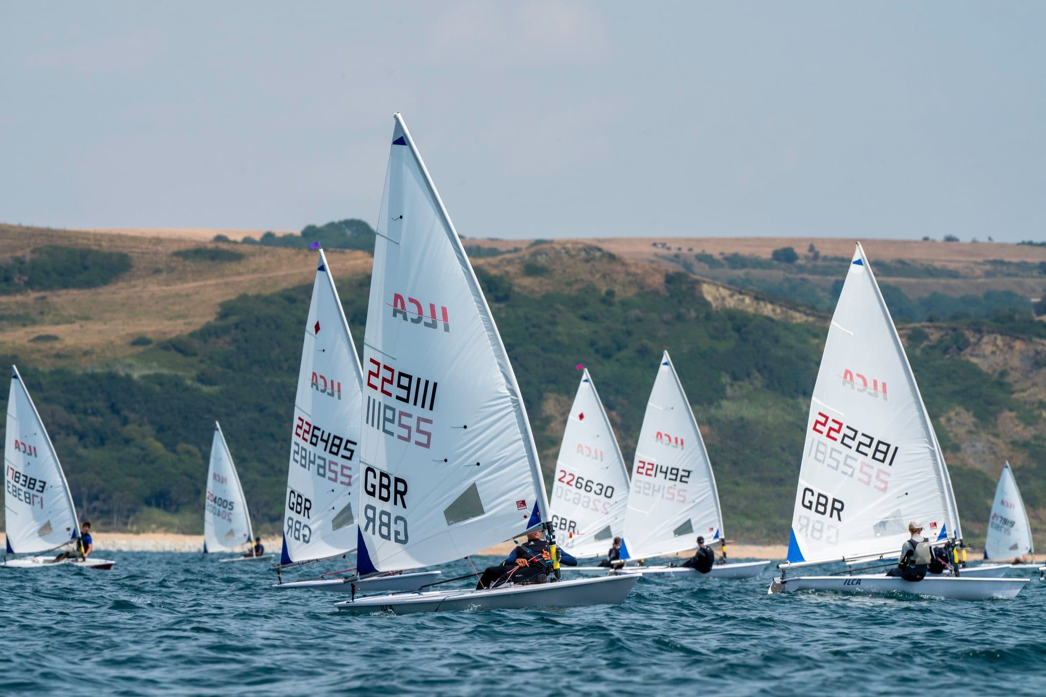 ILCA fleet racing close together off the coastline at the ILCA UK Nationals, photographed by Megan Farrer